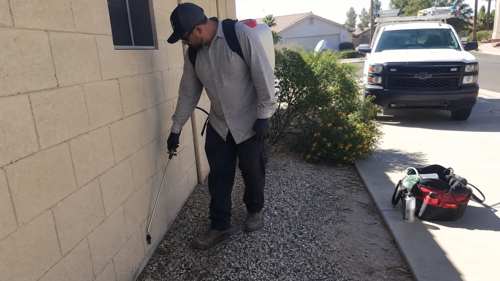 Pest control technician treating the exterior base of a Phoenix block wall